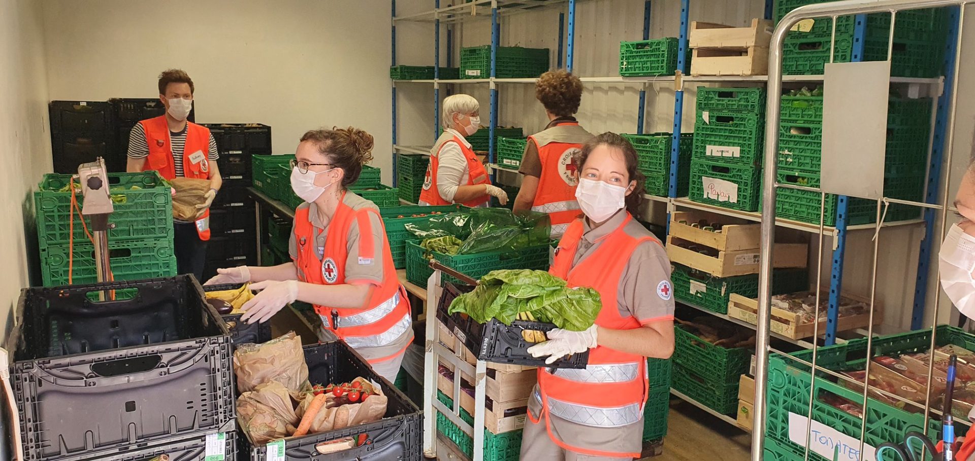 5 Bénévoles de la Croix Rouge transportent des caisses dans un réserve de légumes frais