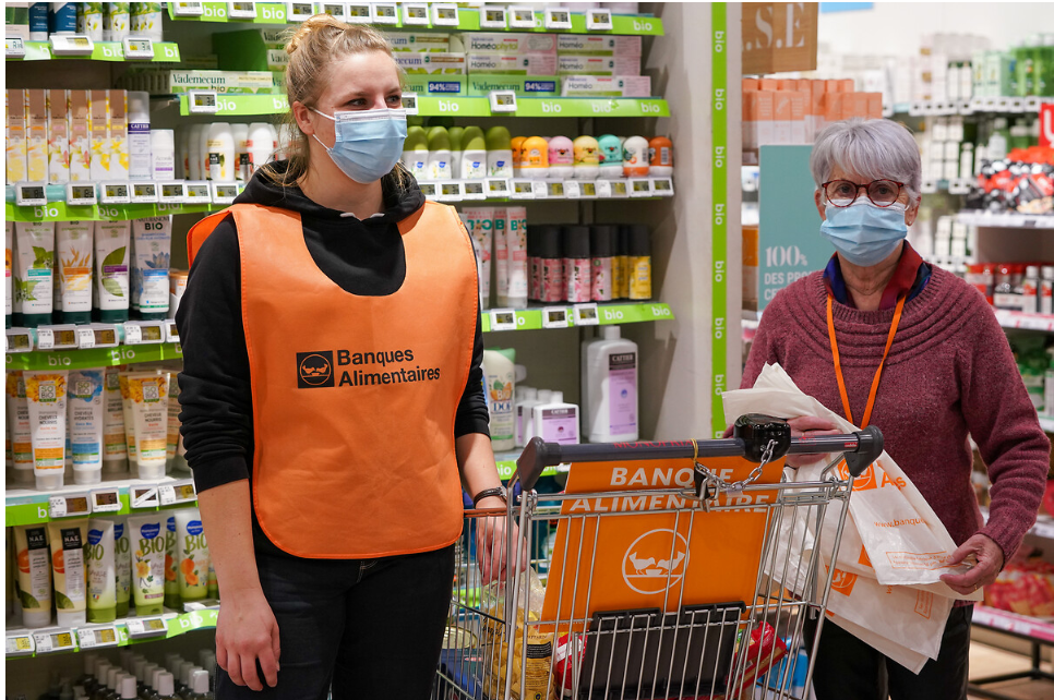 2 femmes bénévoles de la banque alimentaire à côté d'un caddie rempli de produits alimentaires