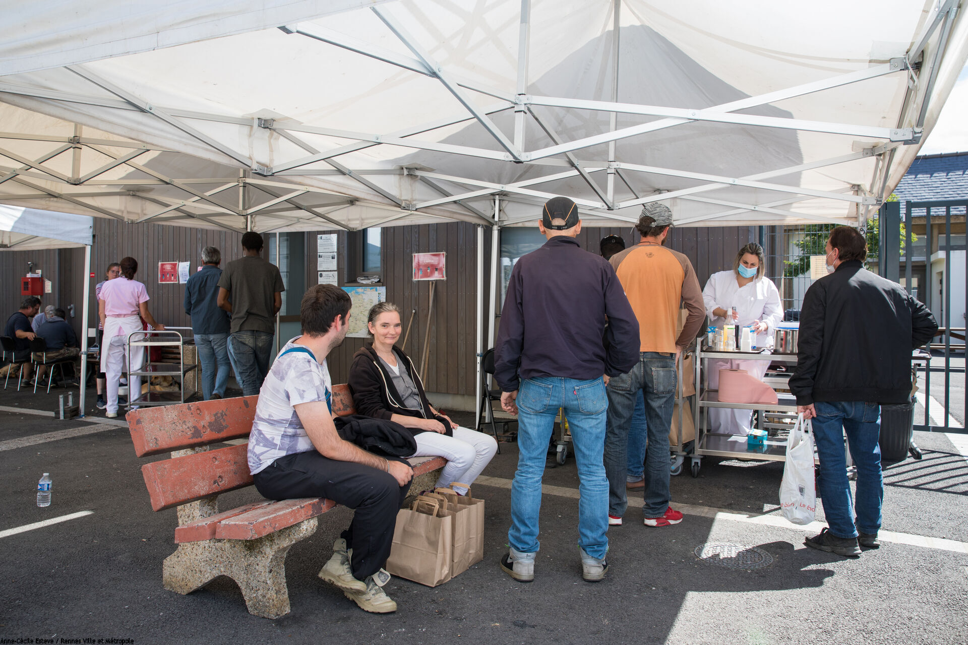 Distribution de boissons par un cantinière à des personnes sans-abri faisant la queue